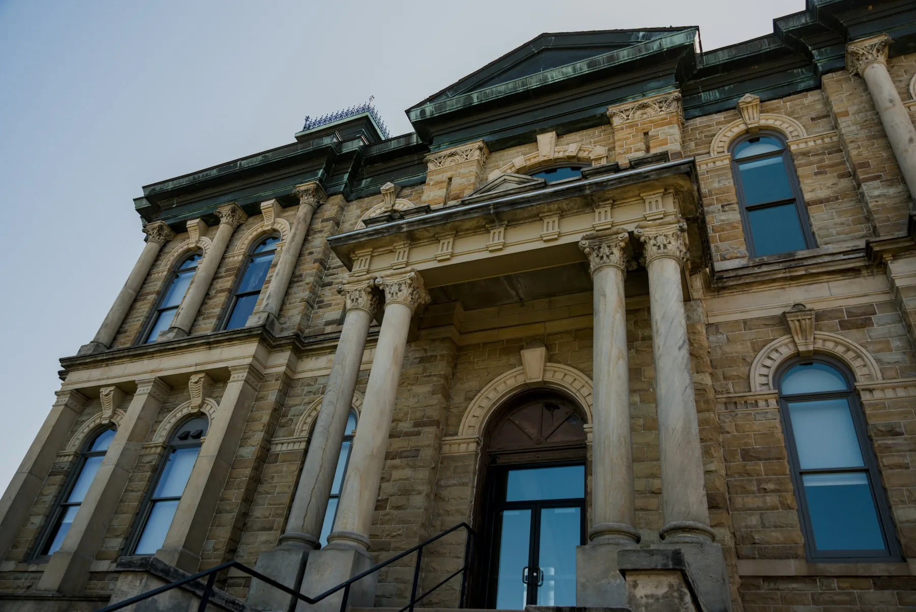 A sandstone county courthouse with tall columns and arched windows, seen from below